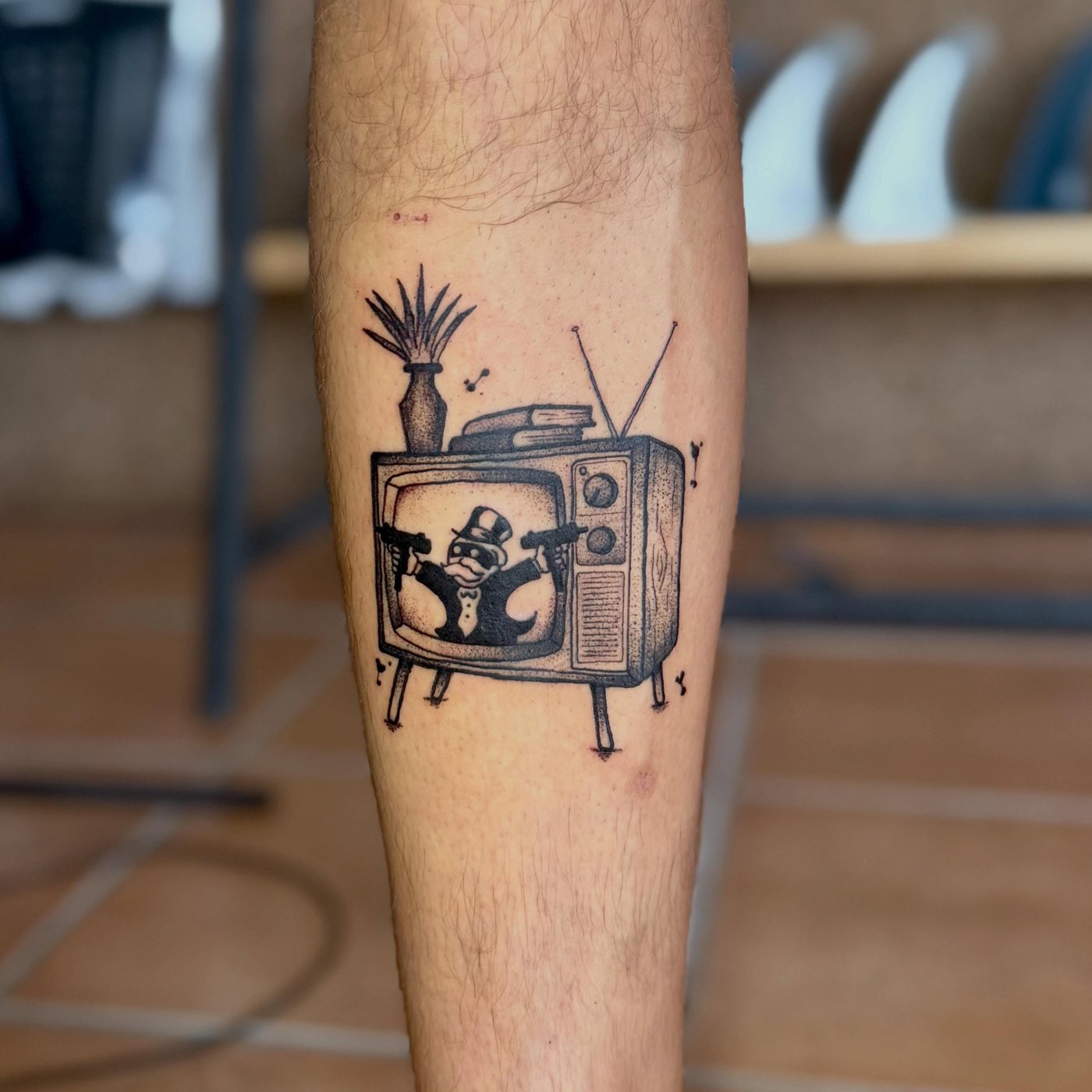 Tatuagem de televisão antiga numa perna, com pranchas de surf ao fundo no estúdio