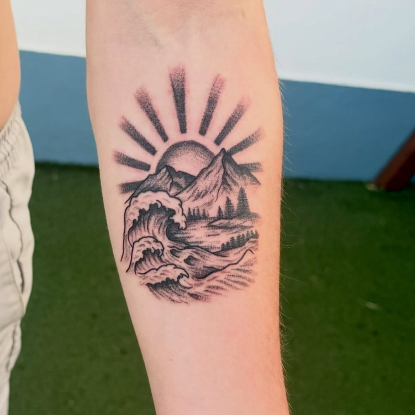 Tatuagem de sol, montanhas e onda em pontilhismo num antebraço